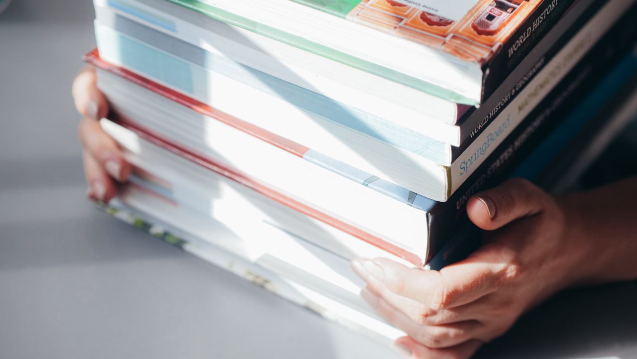 services-01 Close-up of hands holding a stack of colorful books in natural light.